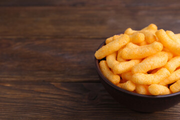 Bowl with crunchy cheesy corn snack on wooden table, closeup. Space for text