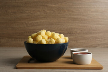 Bowl of corn sticks served with sauces on wooden table, space for text