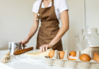 A woman in a special apron cooks at home. Rolling out and preparing dough for baking.