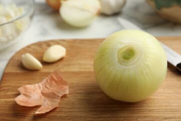 Peeled onion and knife on wooden board, closeup