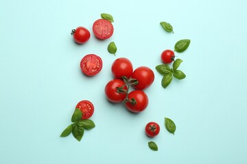 Fresh cherry tomatoes and basil leaves on light blue background, flat lay