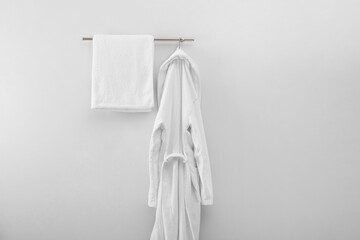 Rack with clean bathrobe and towel on light wall
