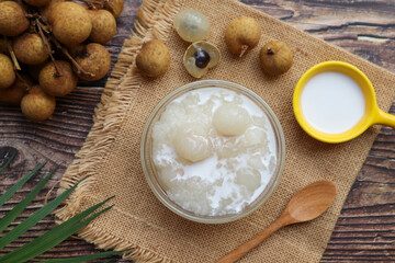 Sticky rice boiled in syrup with longan and coconut milk dressing at top view on wood table - Thai dessert called Kao Nioew Peak LamYai