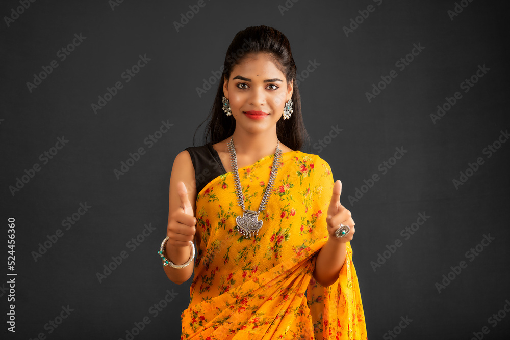 Wall mural Young smiling girl showing ok sign or thumbs up on a grey background