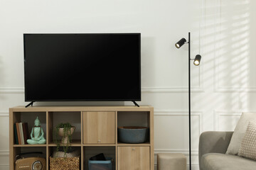 Modern TV on cabinet and lamp near white wall indoors. Interior design