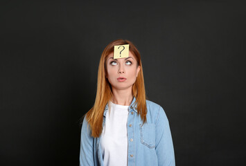 Emotional woman with question mark sticker on forehead against black background