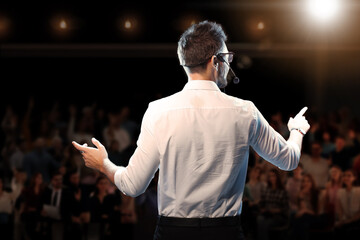Motivational speaker with headset performing on stage, back view - obrazy, fototapety, plakaty