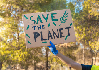 Detalle de mano con pancarta, en una manifestación en la naturaleza, con el mensaje de salvar el planeta. Fotografía horizontal. © Ezequiel Martínez