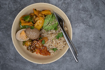 Korean brown rice, kimchi, stir fried vegetables and pickled egg, avocado in a bowl, copy space