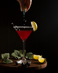 black currant cocktail in martini glass with lime and drops, dark background