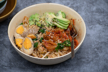 Korean brown rice, kimchi, stir fried vegetables and pickled egg, avocado in a bowl, copy space