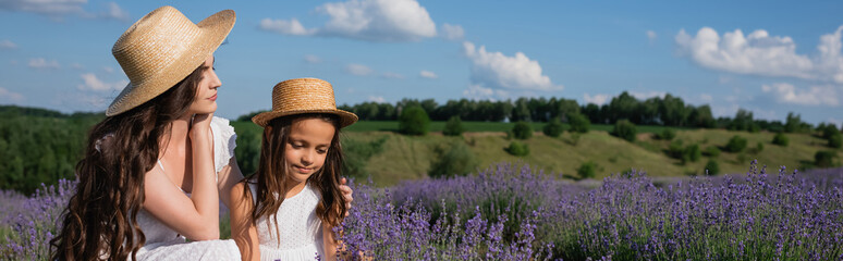 brunette woman in straw hat hugging daughter in lavender meadow, banner.