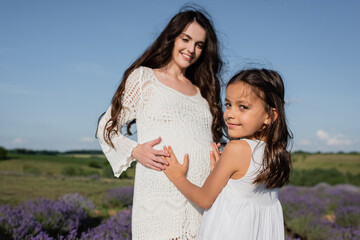 smiling girl embracing tummy of pregnant mother in openwork dress.