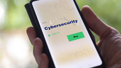 An investor's analyzing the cybersecurity etf fund on screen. A phone shows the ETF's prices stocks to invest in cyber security.