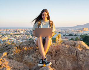 Young woman with a backpack, using a laptop to make a video call in the middle of a field. Digital...