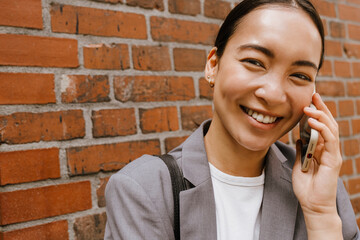 Asian young businesswoman smiling and talking on cellphone on street