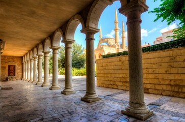 Obraz premium The Mohammad Al-Amin Mosque situated in Downtown Beirut, in Lebanon as viewed through the pillars of the Greek Orthodox church of St George.