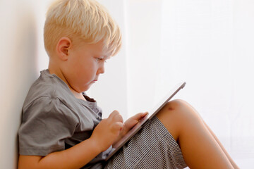 Blondy boy spend his leasure time in tablet