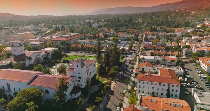 Lovely white houses with orange roofs, numerous cars on the streets and parking lots. Beautiful architecture and hills of Santa Barbara at backdrop of pink skies.