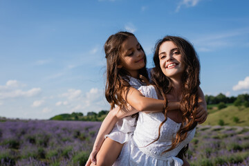 excited woman piggybacking daughter in blurred lavender field.