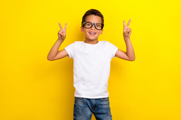Photo of funny little boy show v-sign wear white t-shirt eyewear jeans isolated on yellow color...