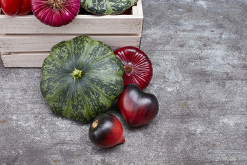 Pine box full of colorful fresh vegetables on a table and gray background. Beautiful irregular shaped vegetables. Food waste from supermarket. Trendy vegetables concept. Selective focus
