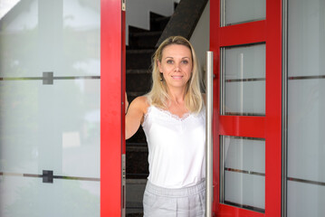 Fototapeta na wymiar Woman looking through a red door with a welcoming smile