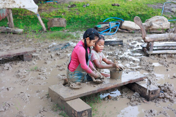 Happy dirty African and Asian girl playing in puddle mud together at outdoor summer camp learning