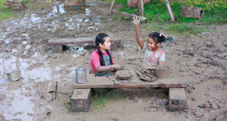 Happy dirty African and Asian girls playing rock paper scissors in puddle mud together at outdoor summer camp learning