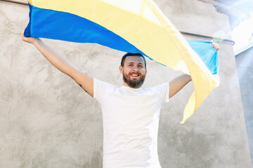 Soft selective focus on Man holding the National Blue and Yellow Flag of Ukraine above his head and smiling. Guy in white T-shirt and jeans. Sunny day. Constitution and Independence Day of Ukraine.