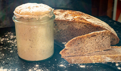 Homemade sourdough starter in glass on dark background and graham bread