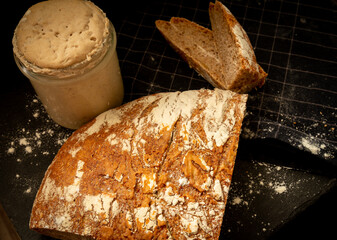 Loaf of artisan wheat and rye bread with graham flour. Sourdough starter on dark background. Top view.