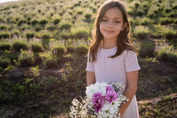 brunette girl with bouquet looking at camera in green field.