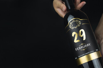 February 29th. Day 29 of month, Calendar date. Hands hold bottle of red wine with a calendar date...