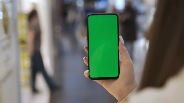 View of a woman on the phone with a green screen for copy space. Chromakey mockup without tracking markers. Close up.Young woman standing in a shopping mall with a smartphone. Busy shopping center