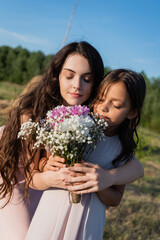 woman and child with closed eyes smelling aromatic flowers in blurred meadow.