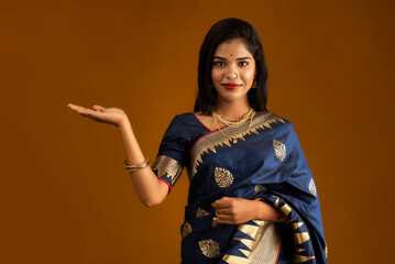 Portrait of Indian traditional young woman or girl presenting something, showing copy space on her palm on a brown background