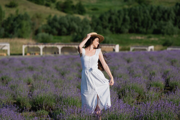 Fototapeta na wymiar woman in white dress and straw hat posing in field with blossoming lavender.