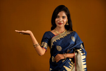 Portrait of Indian traditional young woman or girl presenting something, showing copy space on her palm on a brown background