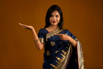Portrait of Indian traditional young woman or girl presenting something, showing copy space on her palm on a brown background