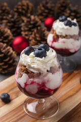 Trifle - traditional English dessert. Two portion in glasses on a dark stone table. Christmas and New Year's composition. Red Christmas balls, pine cones in background. Vertical orientation.