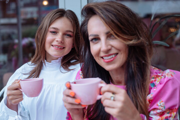 Calm smiling mother and daughter drinking coffee in outdoor cafe, spending time together....
