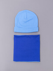 Blue hat and scarf-tube on gray background. Warm set for woman, man or child. Top view