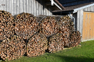 Sawn firewood for residential heating is stacked near the fence.