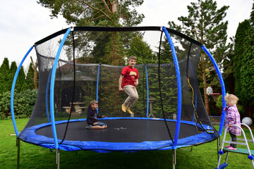 The children bought a new trampoline and put it in the yard and jump on it. - obrazy, fototapety, plakaty