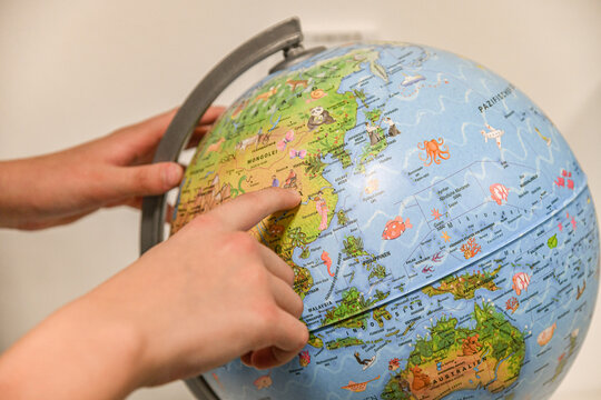 The student boy spins the globe and points to the selected country with his finger.