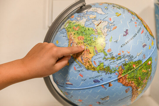 The student boy spins the globe and points to the selected country with his finger. - Powered by Adobe