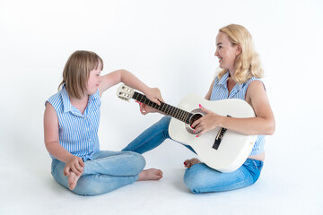 a Teenage Girl  sits on the floor with her mother and plays the guitar in matching shirts on a...