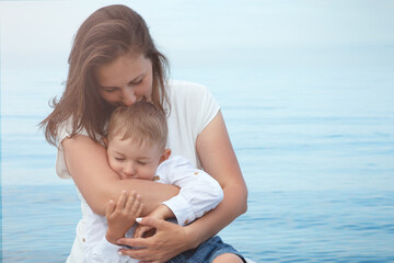 Mom hugs her little son kissing her tightly and lovingly against the background of the sea.