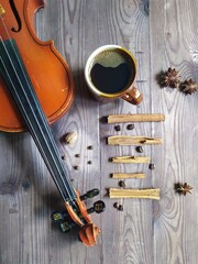 Naklejka premium Musical note chord of cinnamon, coffee beans, star anise, with cup of coffe and violin on brown wooden background, top view